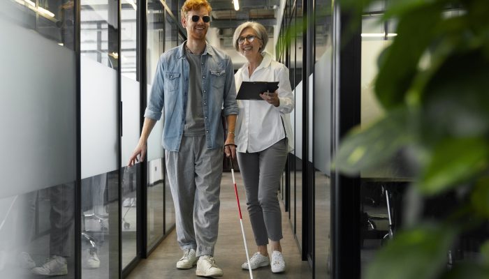 dwie osoby idą korytarzem, j edna z nich jest niewidoma, trzyma w ręku białą laskę