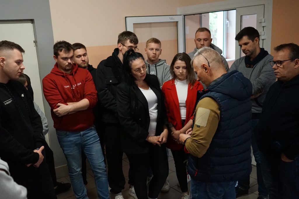 grupa studentów stoi i słucha prowadzącego