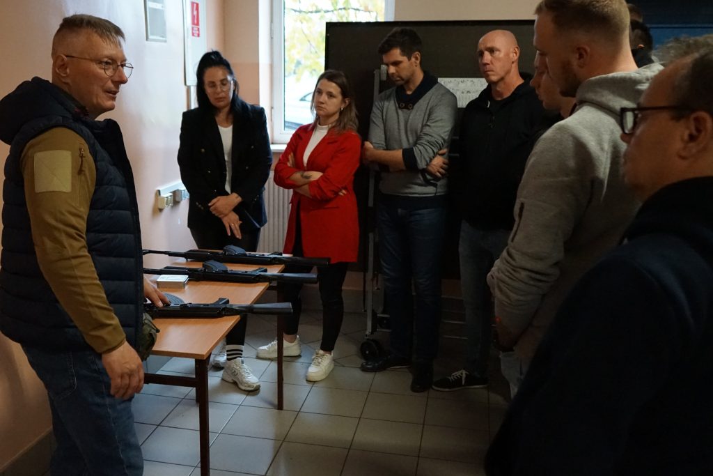 grupa studentów stoi i słucha prowadzącego