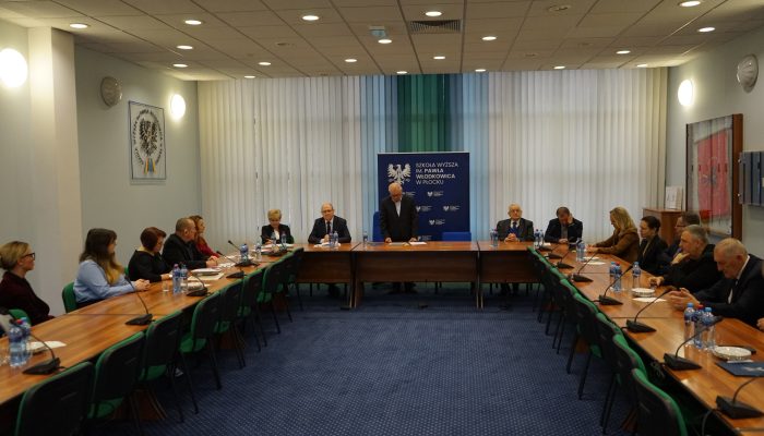 sala ze stołem ustawionym w literę U, siedzą za nim ludzie