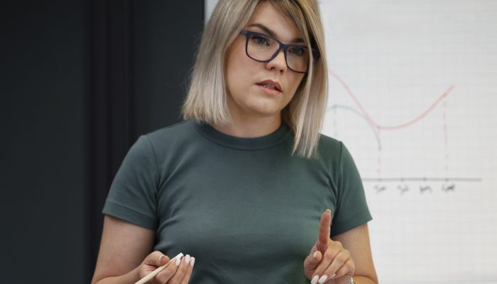 Kobieta prowadząca zajęcia. W prawej dłoni trzyma biały długopis